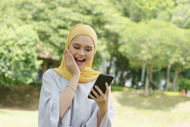 Portrait of cheerful Muslim girl using smartphone, smiling at outdoor. - Фото, зображення