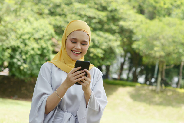 Portrait of cheerful Muslim girl using smartphone, smiling at outdoor. - Valokuva, kuva