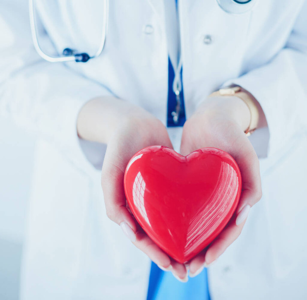 Female doctor with stethoscope holding heart, on light background - Photo, Image