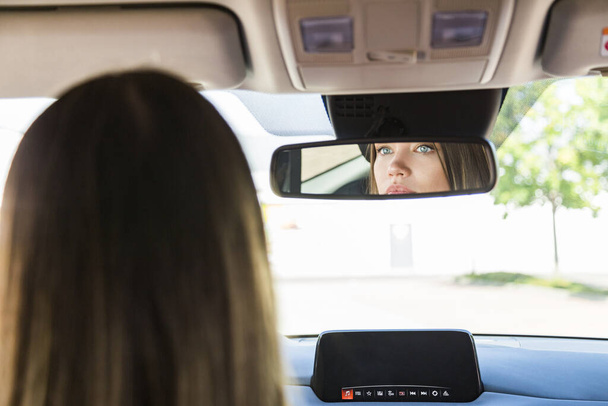 Girl looks in rearview mirror in car and tint lips - Foto, Bild