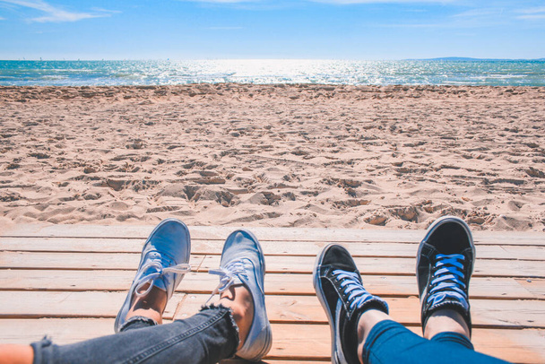 Two pair of shoes at the beach. A couple of people laying at the beach enjoying the sun. - Photo, image