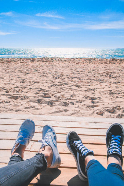 Two pair of shoes at the beach. A couple of people laying at the beach enjoying the sun. - 写真・画像