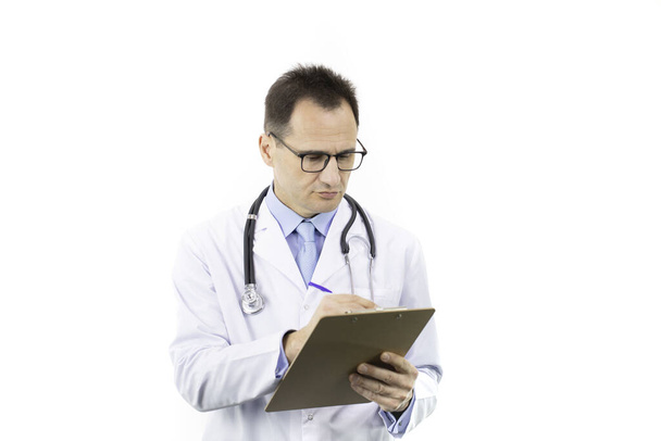 Ernstige arts in witte medische jas en stethoscoop schrijven op klembord - Foto, afbeelding