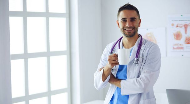 Young and confident male doctor portrait standing in medical office. - Foto, Imagem