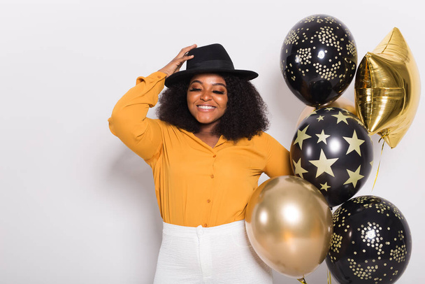 Dovolená, narozeninová oslava a zábavný koncept - Portrét usmívající se mladé afroamerické mladé ženy vypadá stylově na bílém pozadí držící balónky. - Fotografie, Obrázek