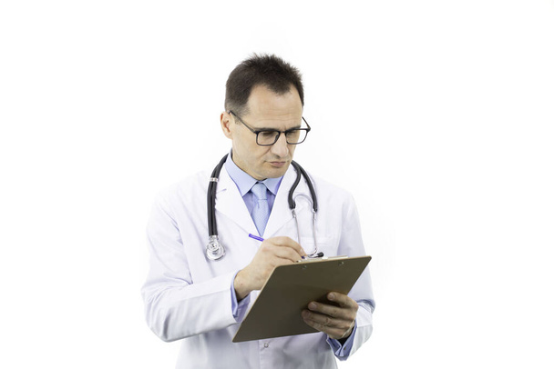 Mooie arts in witte medische jas en stethoscoop schrijven op klembord - Foto, afbeelding