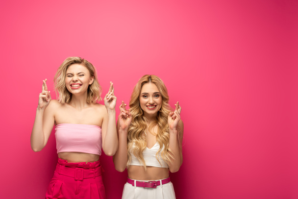Heureux amis blonds avec les doigts croisés sur fond rose
 - Photo, image
