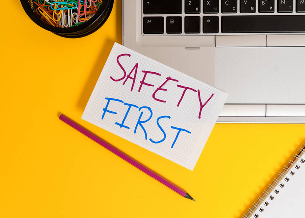 Word writing text Safety First. Business concept for used to say that the most important thing is to be safe Laptop pencil squared paper sheet clips container spiral colored background. - Photo, Image