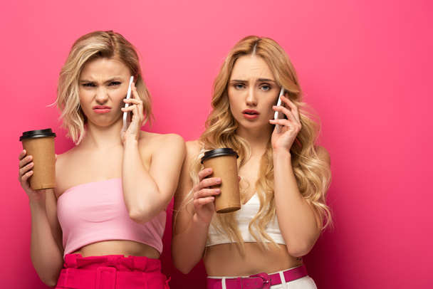 Filles blondes confuses avec des tasses en papier parlant sur les smartphones sur fond rose
 - Photo, image