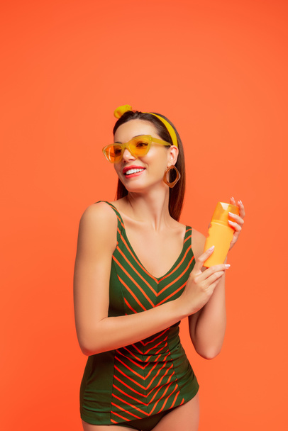 Mujer con protector solar mirando hacia otro lado y sonriendo aislada en naranja
 - Foto, imagen