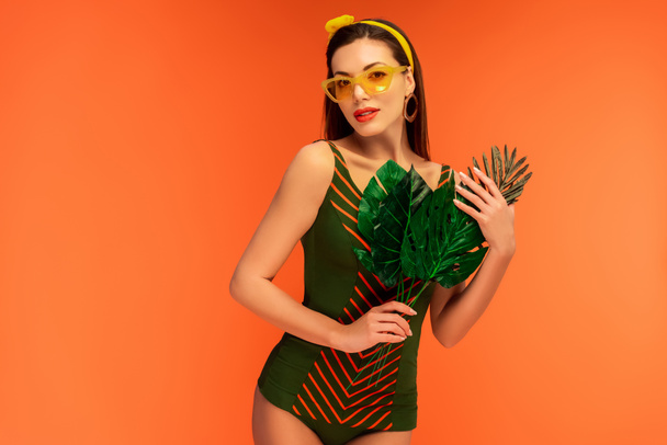Woman holding leaves and looking at camera isolated on orange - Foto, Bild