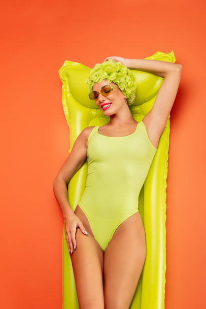 Top view of woman with closed eyes smiling and resting on inflatable mattress on orange background - Photo, Image
