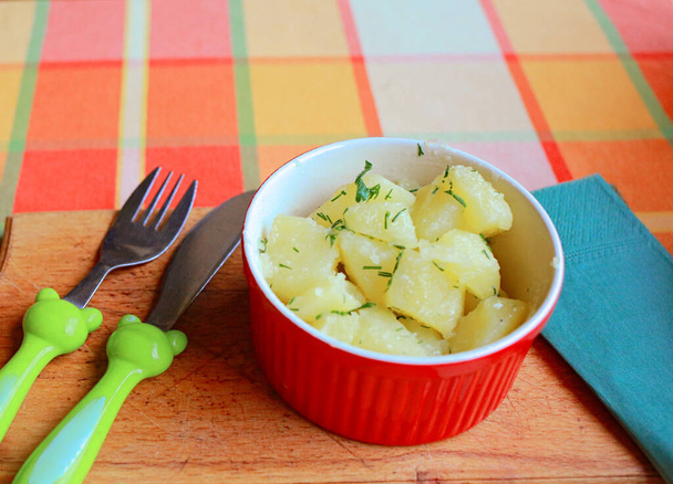  gekochte Kartoffeln mit Kräutern in einem roten Teller auf einem Holzständer, Nahaufnahme, richtige Ernährung - Foto, Bild