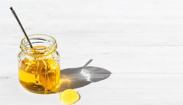 Organikus természetes méz egy üveg üveg fehér fából készült háttér, közelkép. Vintage kanál egy nyitott üvegben mézzel. Fényes napfény ragyog keresztül egy üveg mézen.. - Fotó, kép