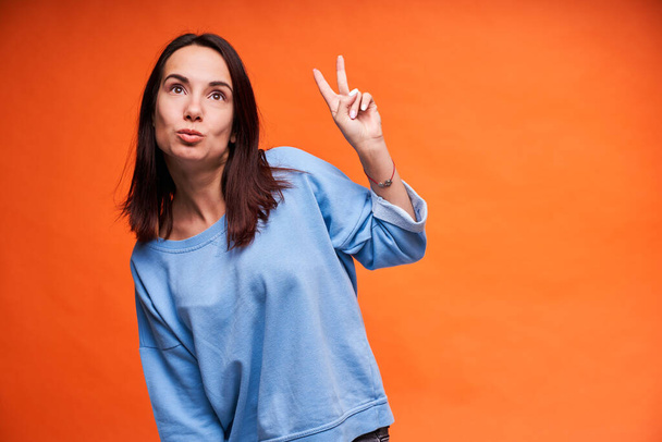 Happy successful young woman with raised arms showing victory on orange background - Photo, Image