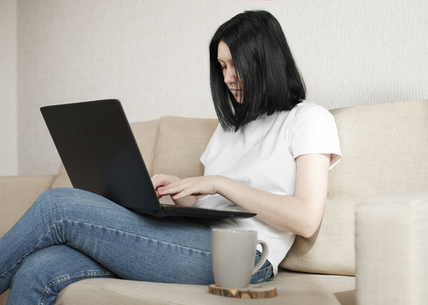 Молодая женщина работает из дома, сидя на диване
.  - Фото, изображение