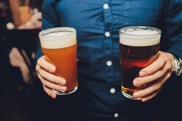 Bir adamın elinde bir bardak bira, elinde bir bardak dolusu bira, bardaki bir adamın elinde leziz, serin, ferahlatıcı barmenlerin çalışmasını kutlarken çekilmiş görüntüsü.. - Fotoğraf, Görsel