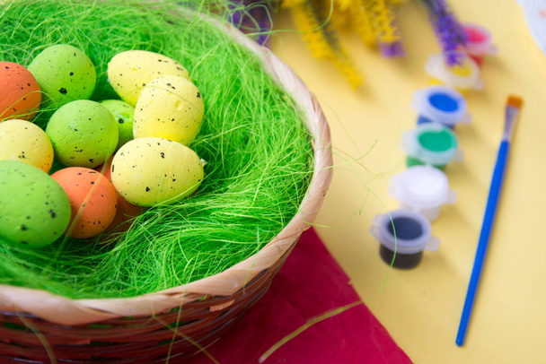 Зелене гніздо в кошику з невеликими барвистими великодніми яйцями, прикраса, крупним планом Великодня концепція, святкова традиція, розмиті фарби та пластикові квіти на жовтому тлі, вибірковий фокус
 - Фото, зображення