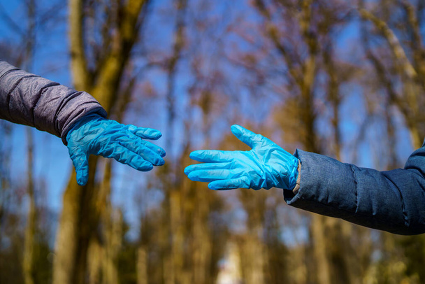 Man and female hands in medical gloves stretch to each other. Park with high trees blurred background. Selective focus. Coronovirus epidemic. COVID-19 and coronavirus identification. Pandemic - Фото, зображення
