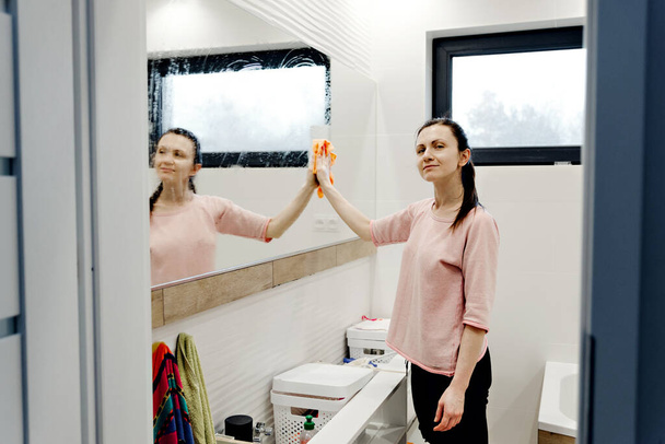 young housewife washes a mirror with detergent,happy woman cleaning mirror with rag at home,pretty woman cleans mirror in bathroom at home,cleaning the bathroom,mirror cleaning - Foto, imagen