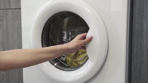 A női kéz ruhákat vesz a mosógépből. Mosógép betöltése. Ruhákat a mosógépbe. Ruha mosógép betöltése. Mosás előkészítése - Felvétel, videó