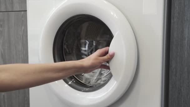 A női kéz fehér ruhákat vesz ki a mosógépből. Mosógép betöltése. Ruhákat a mosógépbe. Ruha mosógép betöltése. Mosás előkészítése - Felvétel, videó