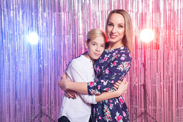 Mothers day, children and family concept - teen boy and his mom embracing on shiny party background. - Fotó, kép