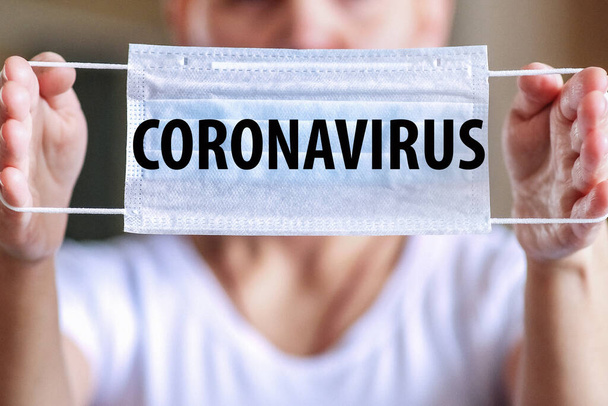 Do not leave the house without a mask. A woman holds a medical protective mask with the words CORONAVIRUS. A woman screams to protect herself from the epidemic. - Photo, Image