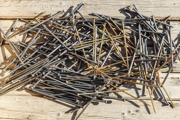 Iron nails and screws on a wooden background. Long, metal, carpenter's nails and self-tapping screws for construction. Fixing tool. The view from the top - 写真・画像