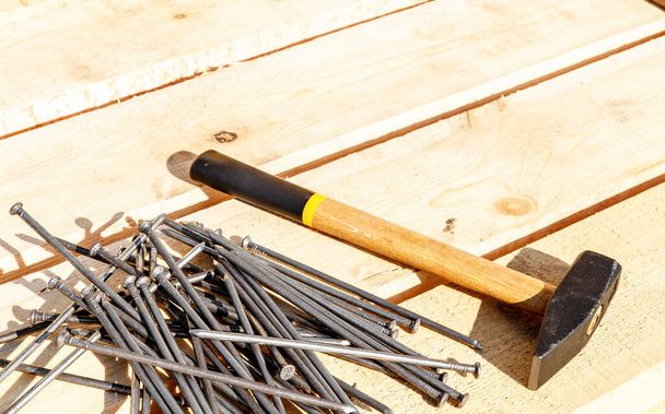Iron nails and a hammer on a wooden background. Long, metal, carpenter's nails and a mallet lie on a bar for construction. Side view. space for text - 写真・画像
