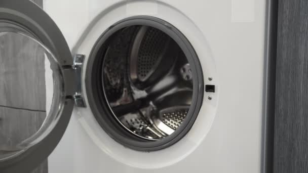 Female hand put WHITE CLOTHES in laundry machine. Loading washing machine. Load clothes to washer machine. Load clothes laundry washing machine. Preparing laundry washing - Footage, Video