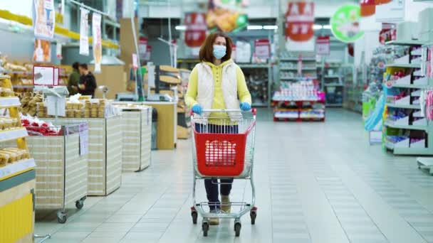 Housewife wearing medical mask and gloves with cart shopping in supermarket - Footage, Video