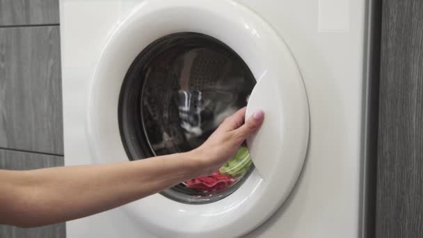 女性の手は洗濯機からカラーの服を取ります。洗濯機を搭載。洗濯機に衣類をロードします。衣類洗濯機をロードします。洗濯の準備 - 映像、動画
