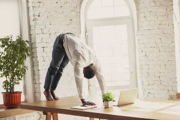 Young african-american man doing yoga at home while being quarantine and freelance working - Fotografie, Obrázek