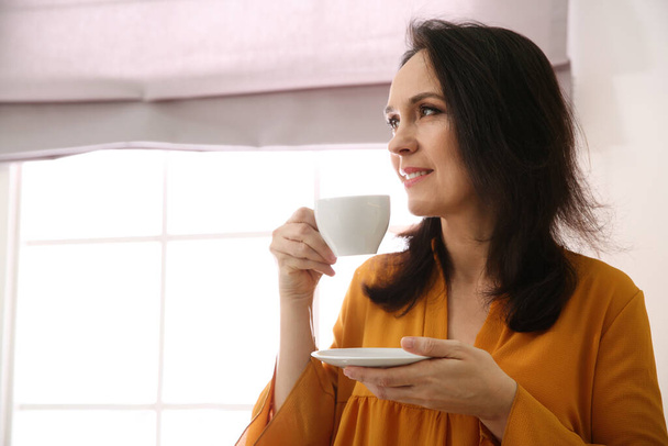 Beautiful mature woman with cup of coffee at home. Space for text - Photo, image