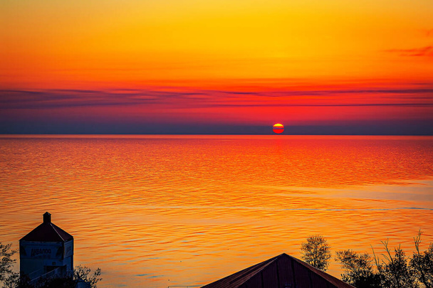 The sun is sinking into the sea and a crimson sunset has filled the entire sky. The sea is calm and quiet, reflecting the bright colors of the sky. - Photo, Image