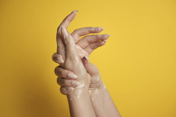 Soapy female hand on a yellow background - Foto, afbeelding