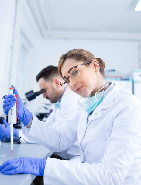 Δύο βιολόγοι άνδρες και γυναίκες ερευνούν δείγματα στο εργαστήριο - Φωτογραφία, εικόνα