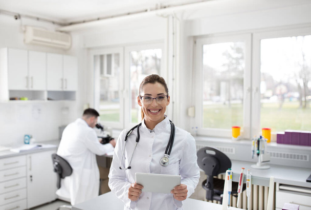 Портрет уверенной женщины-врача с табличкой, стоящей в лаборатории
 - Фото, изображение