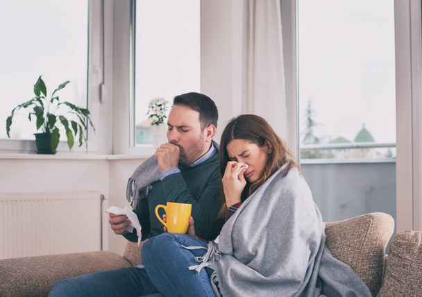 Young couple having virus or flu, covered with blanket sitting on sofa in home isolation during pandemic - Fotoğraf, Görsel