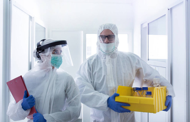 Koruyucu giysiler içindeki iki biyolog laboratuvar koridorunda numune taşıyor. Biyolojik tehlike ve güvenlik kavramı - Fotoğraf, Görsel