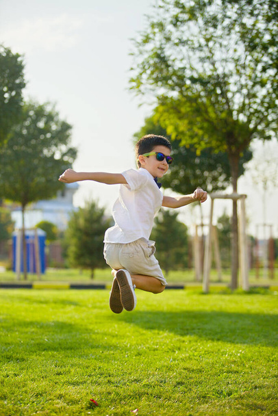 De jongen springt in het park op het groene gras. Het begrip sport en recreatie. - Foto, afbeelding