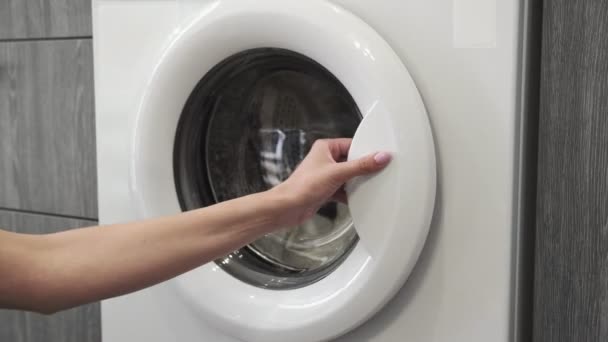 Női kéz, házas gyűrűvel, fehér ruhákat vesz ki a mosógépből. Mosógép betöltése. Ruhákat a mosógépbe. Ruha mosógép betöltése. Mosás előkészítése - Felvétel, videó