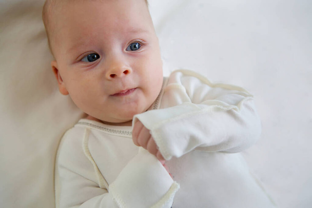 Маленький новорожденный мальчик лежит в белой одежде на белом фоне одеяла
. - Фото, изображение