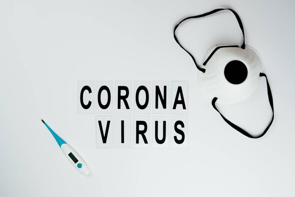 μαύρη επιγραφή coronavirus σε λευκό φόντο και θέση για κείμενο σε λευκό φόντο witn termometer και μάσκα - Φωτογραφία, εικόνα