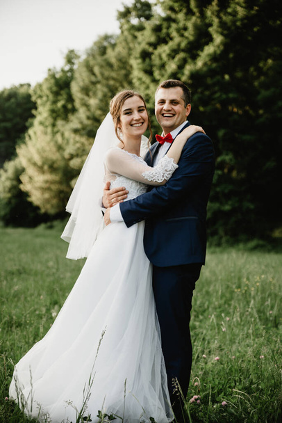 Bride and groom hugging at sunset.Happy bride and groom smiling.Happy bride and groom after the wedding ceremony.Wedding day.Beautiful young couple in a field with flowers,young couple in the forest,bride and groom in nature - Zdjęcie, obraz