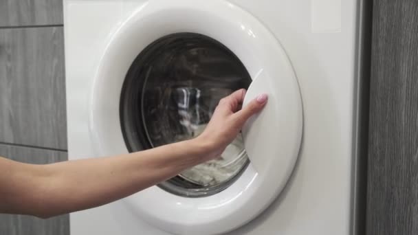 Γυναικείο χέρι με παντρεμένο δαχτυλίδι παίρνει λευκά ρούχα από το πλυντήριο. Φόρτωση πλυντηρίου. Φόρτωσε ρούχα στο πλυντήριο. Φορτώστε ρούχα πλυντήριο ρούχων. Προετοιμασία πλυσίματος ρούχων - Πλάνα, βίντεο