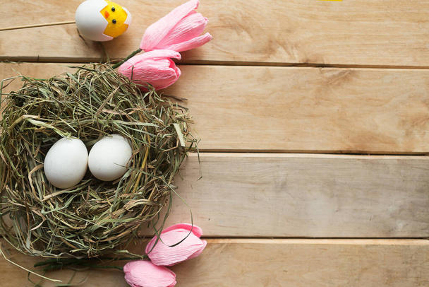 Huevos en nido de heno y tulipanes sobre fondo de madera. Concepto Pascua
 - Foto, Imagen