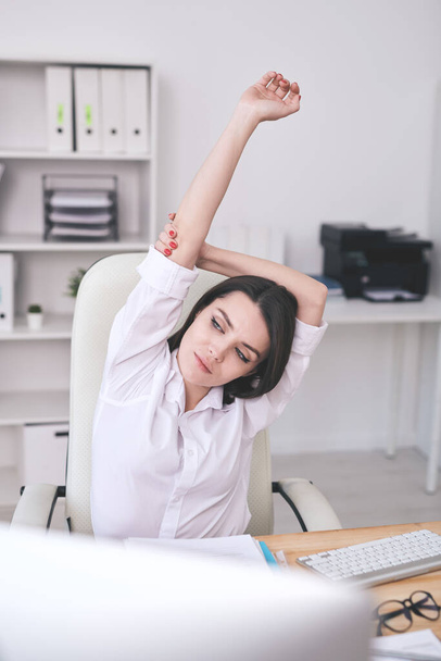 Calmo atraente jovem empresária em camisa branca que se estende na mesa enquanto faz uma pausa no local de trabalho
 - Foto, Imagem