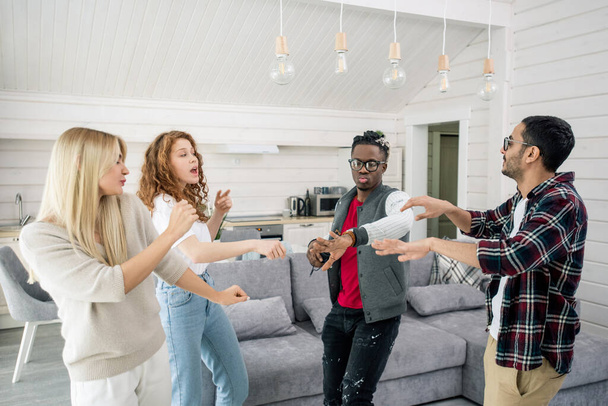 Two young intercultural couples enjoying dancing together in living-room at home party on background of couch and kitchen - Foto, Bild